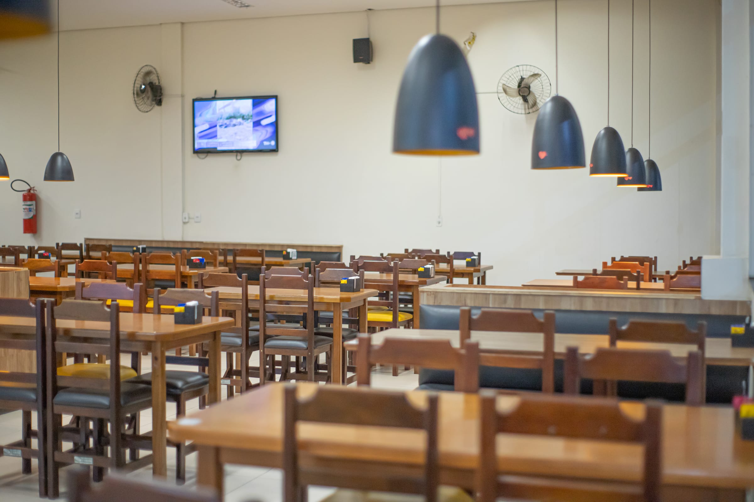 Salão amplo com mesas de madeira e luminárias pendentes