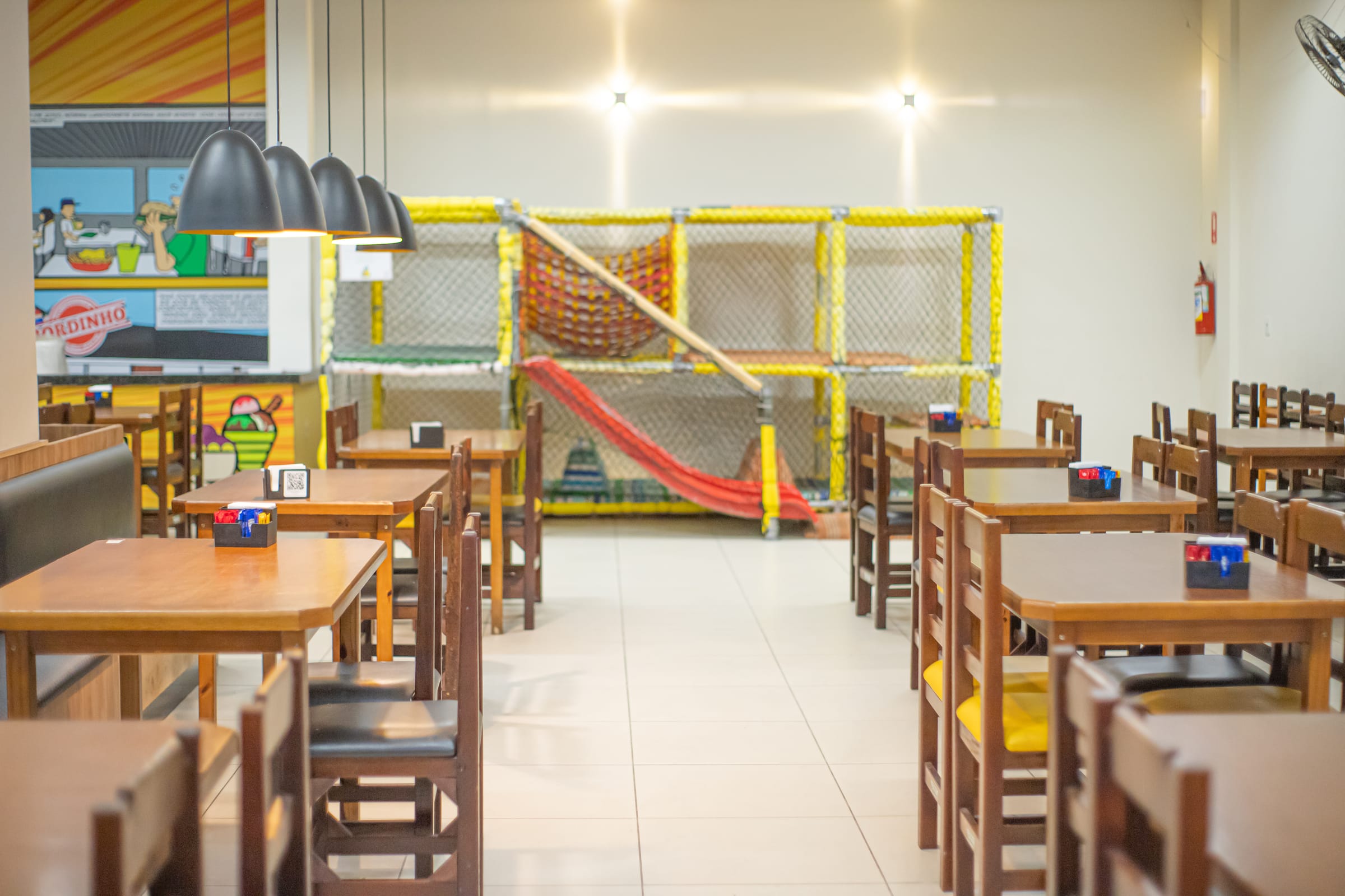 Salão com mesas e o playground infantil ao fundo